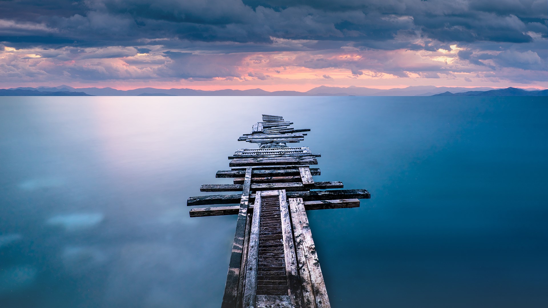 A weathered wooden pier stretching into a calm sea at sunset